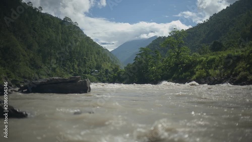 Muddy River Rapids Flowing Through Mountain Valley with Large Boulders