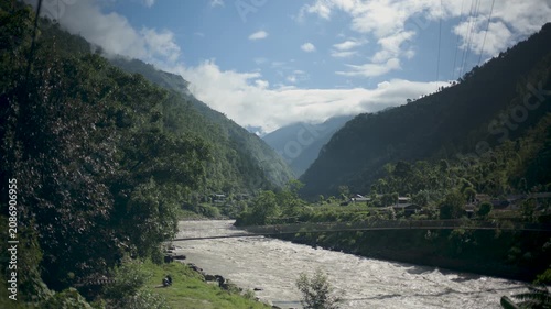 Panoramic View of Rushing Silty Mountain River Flowing Under Blue Sky and Clouds