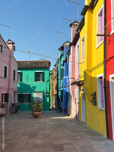 Row of vibrant pink, light blue and orange houses along a traditional narrow street. Burano Island, Italy