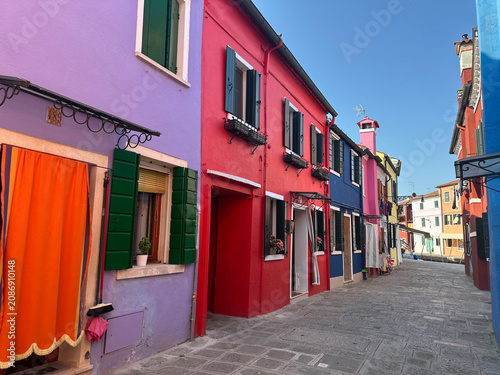 Row of vibrant pink, light blue and orange houses along a traditional narrow street. Burano Island, Italy