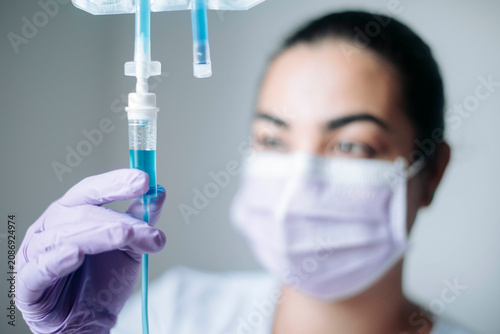 Female healthcare professional inspecting an intravenous drip chamber before patient treatment.
