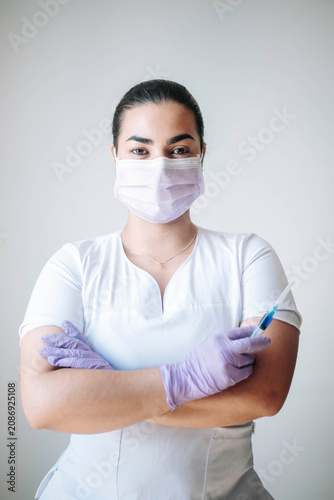 Portrait of a female nurse holding protective gloves while standing confidently in a bright healthcare setting.