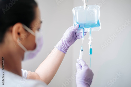 Rear view of a nurse adjusting an IV infusion bag in a bright hospital environment.