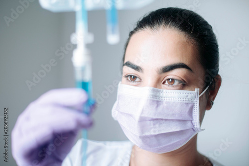 Female nurse monitoring an intravenous IV drip during patient treatment in a healthcare facility.
