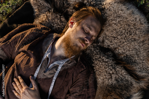 Φωτογραφία A bearded man wearing a tunic rests peacefully on a fur pelt outdoors