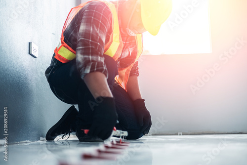 Canvas Print A worker in a safety vest and black gloves uses a tile leveling plier tool to adjust red wedges on a floor, installation and professional interior renovation