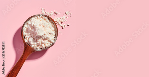 Measuring spoon with collagen powder or alginate mask on pink background.