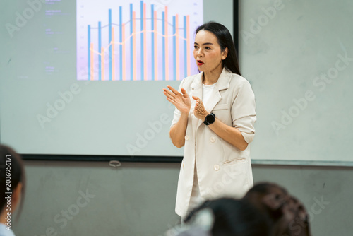 Female professor delivering an engaging academic lecture with crisp data charts on a projector screen to focused university students in a modern classroom