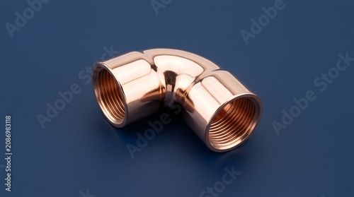 Shiny polished copper elbow pipe fitting with threaded interior segments resting on a smooth dark blue surface for plumbing construction