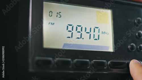 Macro of a finger cycling through FM and SW radio bands on a digital receiver. The backlit LCD screen displays changing frequencies and a signal strength indicator for each mode.