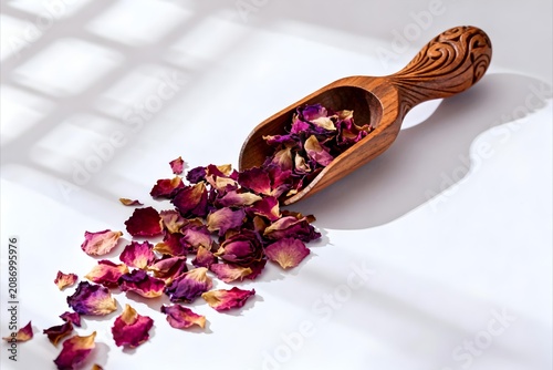 Botanical composition featuring richly colored dried rose petals spilling gracefully from an artisan carved wooden spoon
