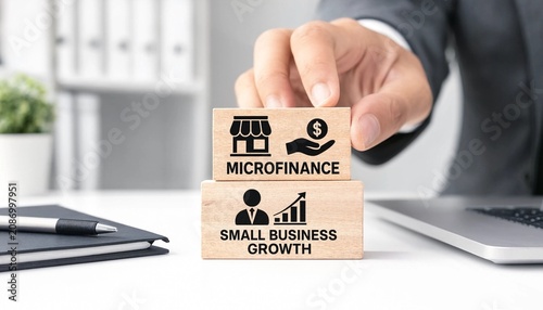 Man placing wooden block with microfinance concept on top of small business growth block on office desk with laptop and notebook
