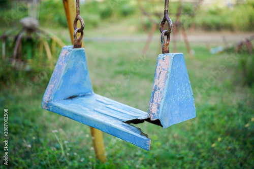 Broken plastic children's swing on the playground, old and unsafe swing. Old blue swing in an abandoned outdoor playground rustic environment