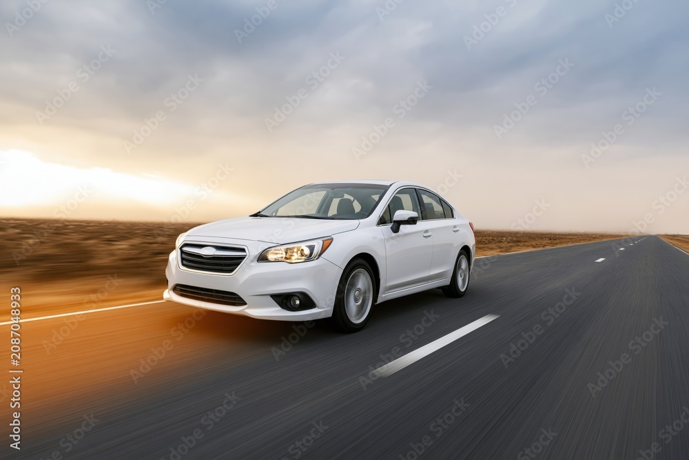 Fototapeta premium The White Sedan Driving Down an Open Highway at Sunset