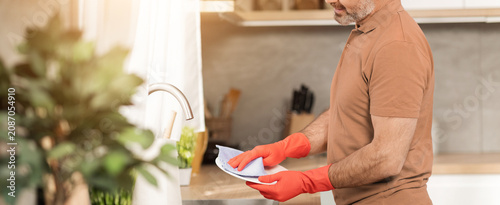 Photos Focused Middle Aged Man Wearing Rubber Gloves While Cleaning Dishes In Kitchen, Engaged In Household Chores