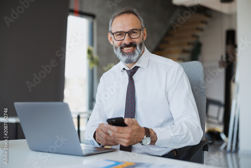 Принти на полотні Confident mid-adult business manager analyzing project data on a computer inside a corporate workspace