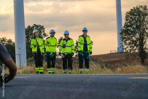 Картината върху платно The wind farm crew of four pause to admire a rotor against the sunset on the park road under fading skies in pink pastel dusk at a wind power plant in Southeast Asia