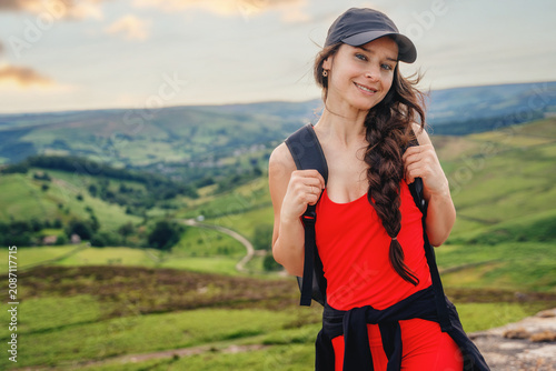 Woman stands on a hill smiling during a hike in a green landscape with hills and valleys in the background near sunset