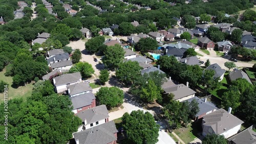 Winding residential streets line heavily treed greenbelts. Gray shingles and brick exteriors stand out against manicured grass, presenting planned community infrastructure in Flower Mound, Texas