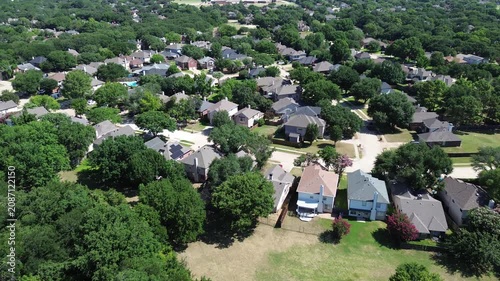 Established neighborhoods feature houses facing large wooded tracts. Dark shingle roofs sit against bright green lawns dense forest borders, showcasing typical residential life in Flower Mound, TX