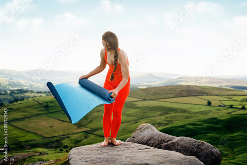 Photos Woman unrolling a yoga mat on a hilltop during a sunny day surrounded by green f