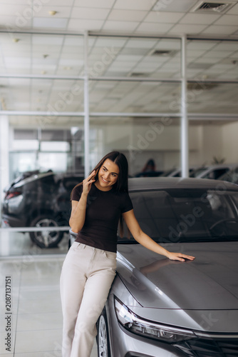 Woman talking on phone leaning on car in showroom