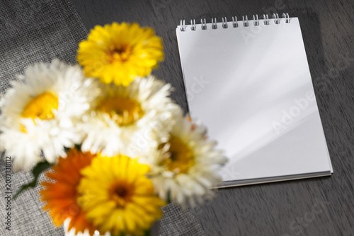Blank notebook and a summer bouquet of double daisies and calendulas on a gray wooden table.