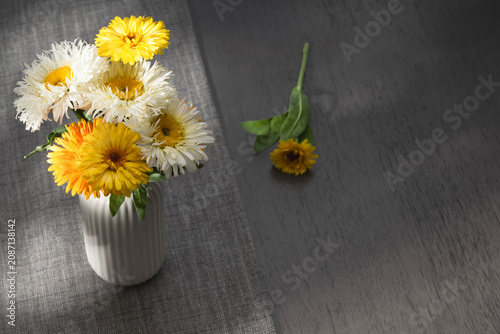 Bouquet of yellow marigolds and white daisies in a ceramic vase on a dark wooden gray table with copy space.
