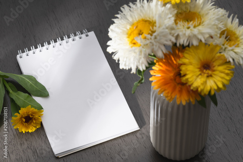 A blank notebook and an orange marigold flower on a gray wooden table.