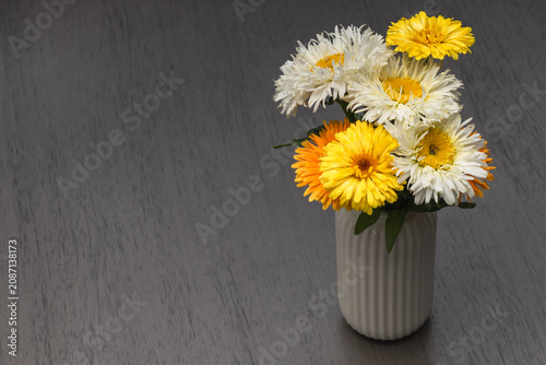 Bouquet of yellow and white flowers in a ceramic vase on a dark wooden table with space for text.