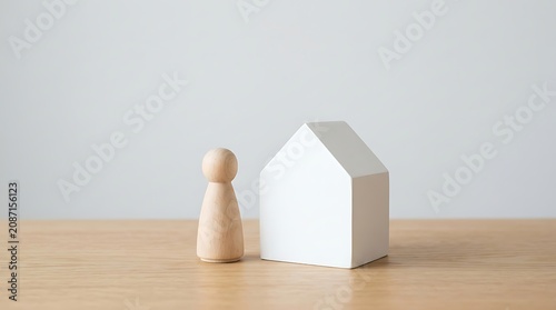 Wooden figure standing next to white house model on table light wood gray wall