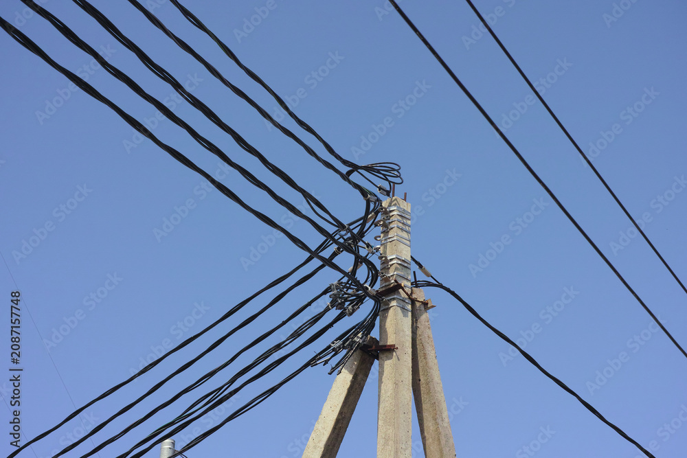 Fototapeta premium Low-angle shot of a concrete utility pole with a complex tangle of black electrical power lines against a clear blue sky background.