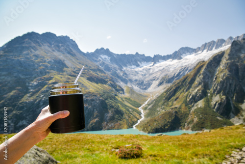 Hand holding a thermal food flask in the mountains