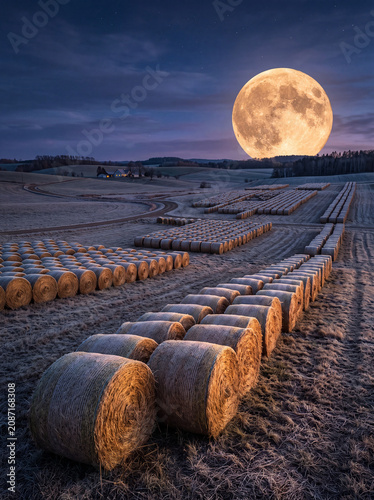 Harvest moon above hay bales in rural farmland at night landscape photography