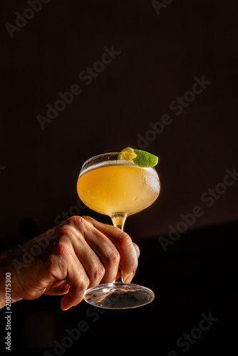 Whisky sour cocktail in glass held by male hand on black background with copy space, dramatic studio lighting, minimal luxury composition.