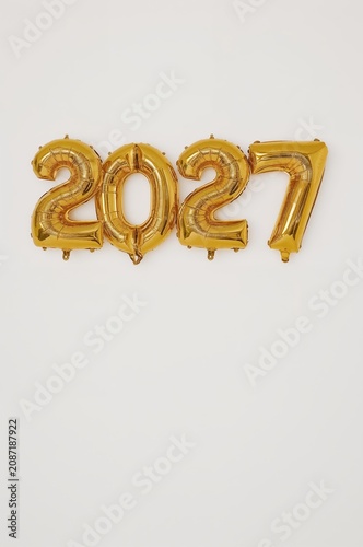 Gold Balloons Displaying the Year 2027 Hang on a White Wall During a Celebrat...