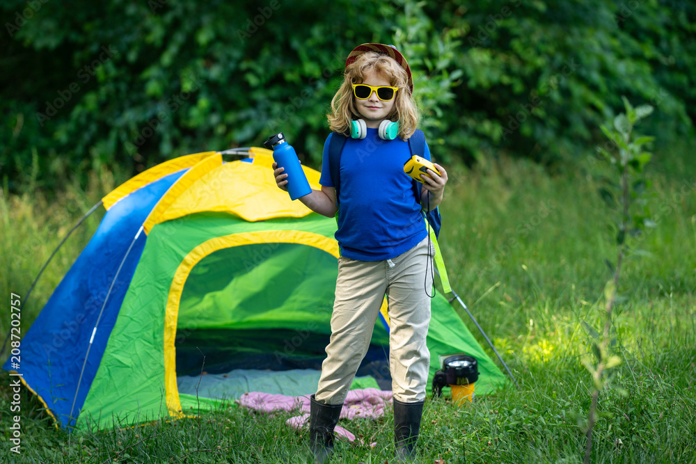 Fototapeta premium Kid exploring nature outdoors. Child hiking in the forest. Kid on camping. Little traveler. Child tourist near tent outdoor. Little explorer with camping gear. Hiking. Child exploring nature at camp.