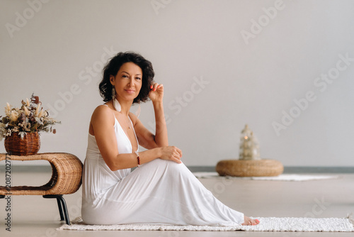 Bild auf Leinwand a woman in a white sundress in a bright interior is sitting on a white rug