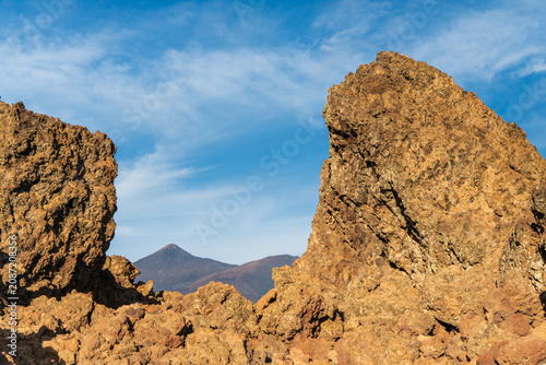 Dramatic volcanic rock formations frame Mount Teide under a clear blue sky