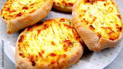 Four khachapuri cooling on dotted plate with bubbling browned cheese and risen crusts under soft diffused light, showing melting surfaces, rich texture, and fresh homemade comfort