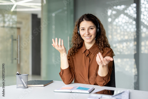 Young female call center agent wearing headset and smiling while providing effective customer support and helping clients in a modern office environment