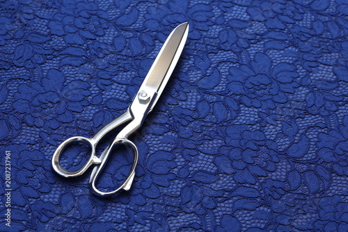 Fotografie Professional tailor scissors on affordable thin royal blue stretchy lace fabric featuring an elegant, intricate floral pattern