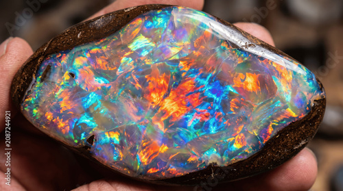 A person holds a piece of opal showing bright colors and patterns. The opal has blues, oranges, and whites