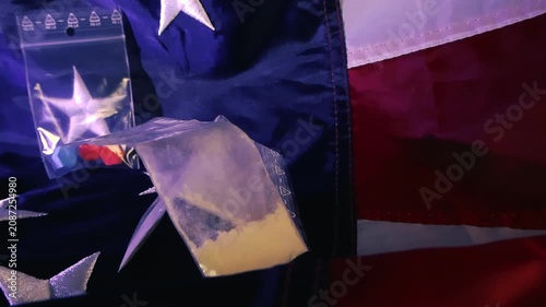 Close up shot of small plastic zip lock bags containing what appears to be narcotics like cocaine and ecstasy pills, lying on an American flag, symbolizing the drug crisis in the USA
