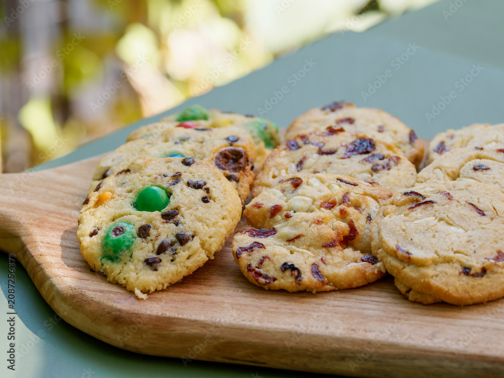 Fototapeta premium Main servant un assortiment de cookies artisanaux sur une planche en bois lors d’un buffet de desserts ou d’un événement en extérieur