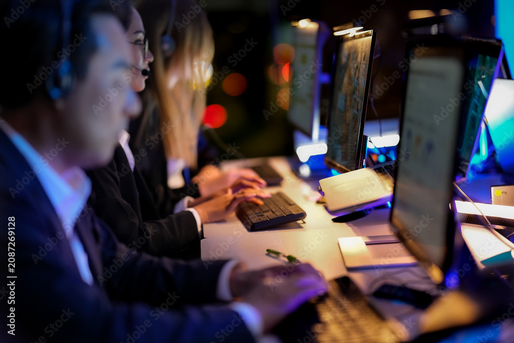 Fototapeta premium Group of coworkers concentrating on a screen in the dark in a blue-lit data center, deep in concentration, in a scene about coding and cool cinematic glow in a professional setting.
