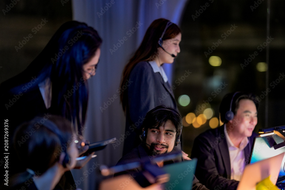 Fototapeta premium Team of consultants checking a smartphone lit by its screen in a dimly lit software studio, solving a problem together, in a scene about innovation and focused late-night mood.
