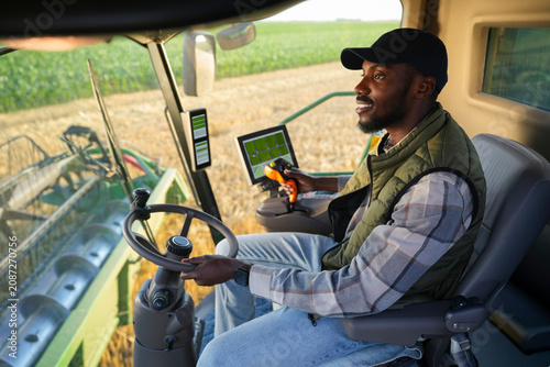 Tableau sur toile A farmer drives a large harvester in a field with green crops