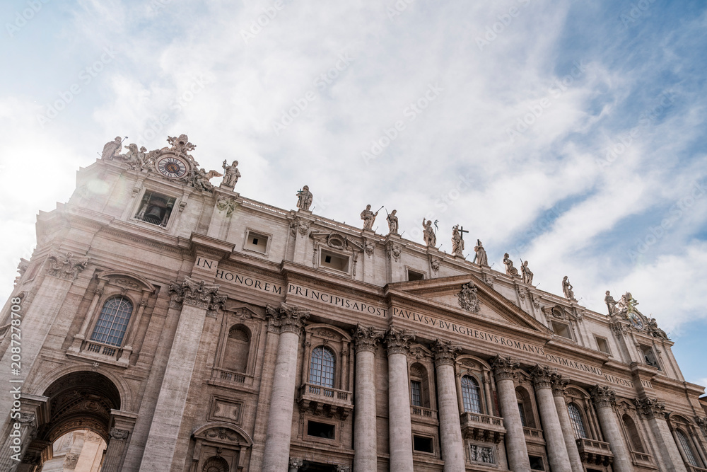 Fototapeta premium Low-angle view of ornate basilica facade with classical statues and columns under a cloudy sky