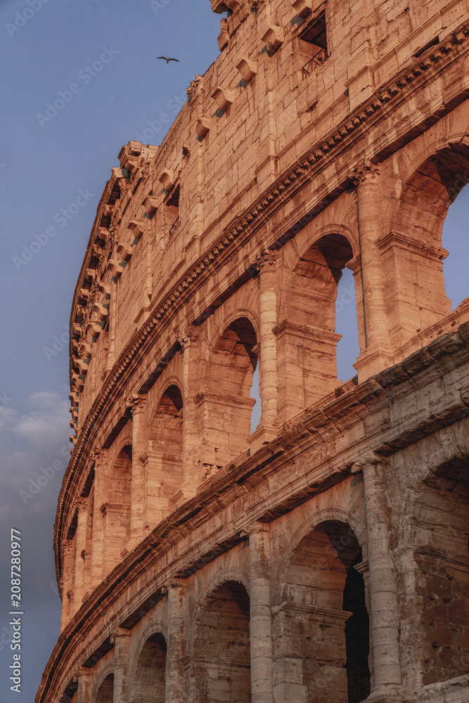 Fototapeta premium Exterior detail of the Colosseum amphitheater in Rome at golden hour showing ancient stone arches and sky